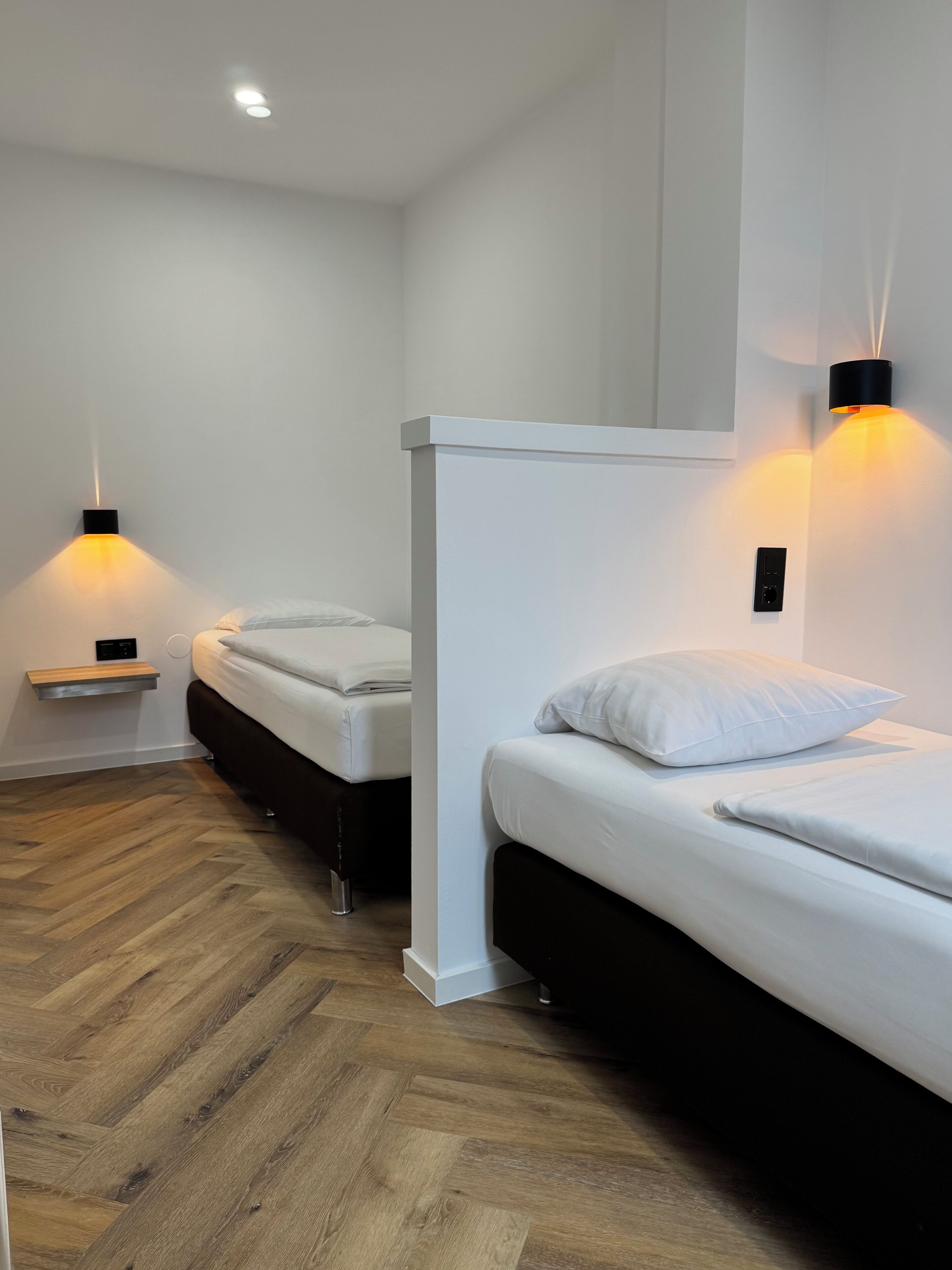 Una habitación de hotel moderna con dos camas, suelo de madera e iluminación en la pared.
