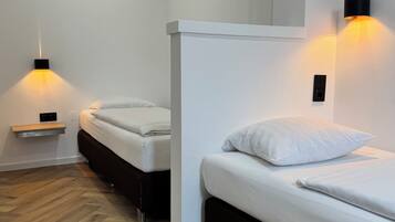 Una habitación de hotel moderna con dos camas, suelo de madera e iluminación en la pared.