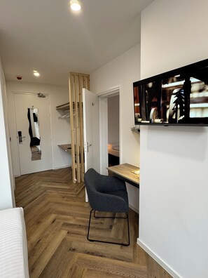 Una habitación moderna con suelo de madera en espiga, una silla gris, un escritorio de madera y un televisor fijado a la pared.