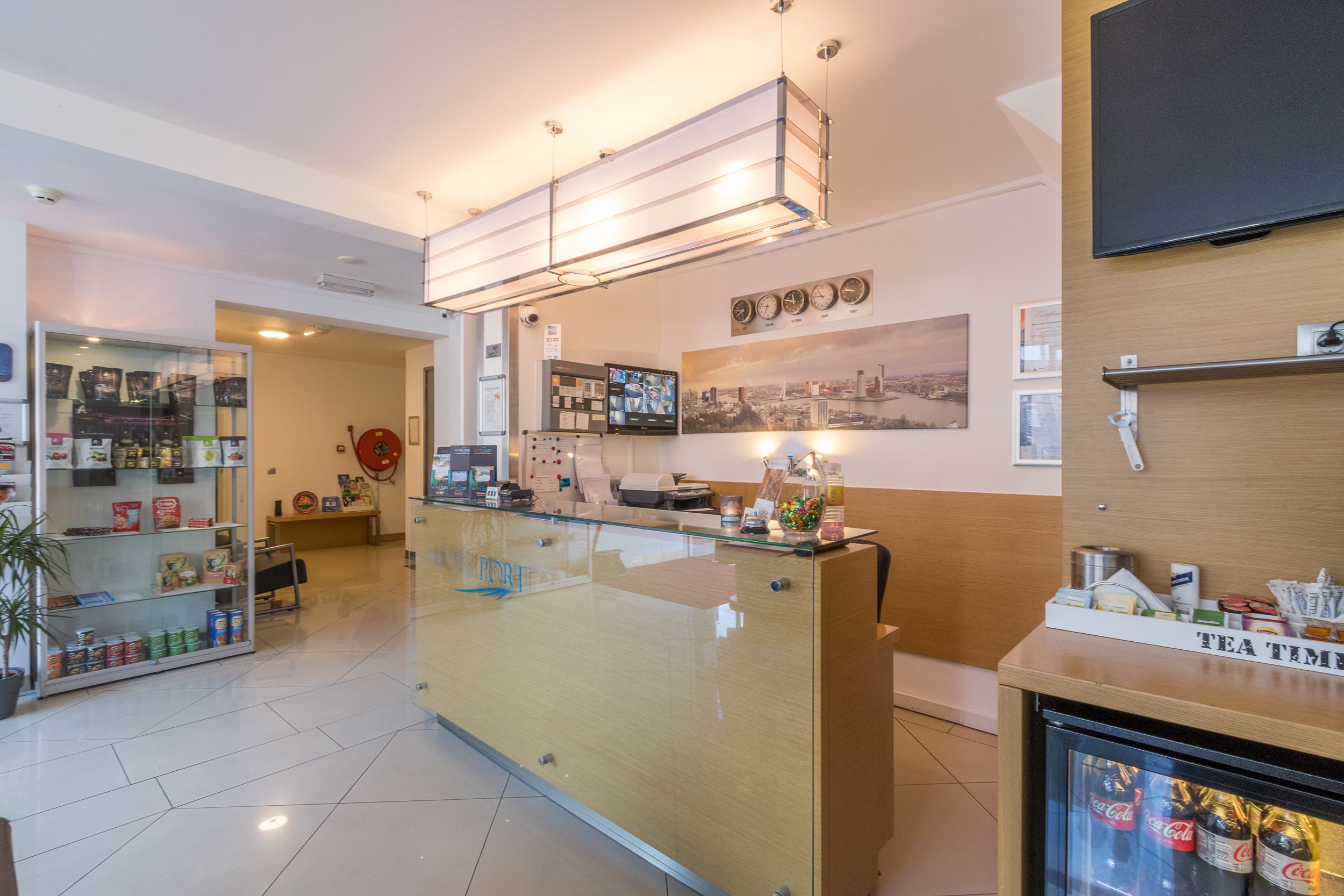 Zona de recepción con mostrador de cristal, refrigerador con bebidas y televisor instalado en la pared.