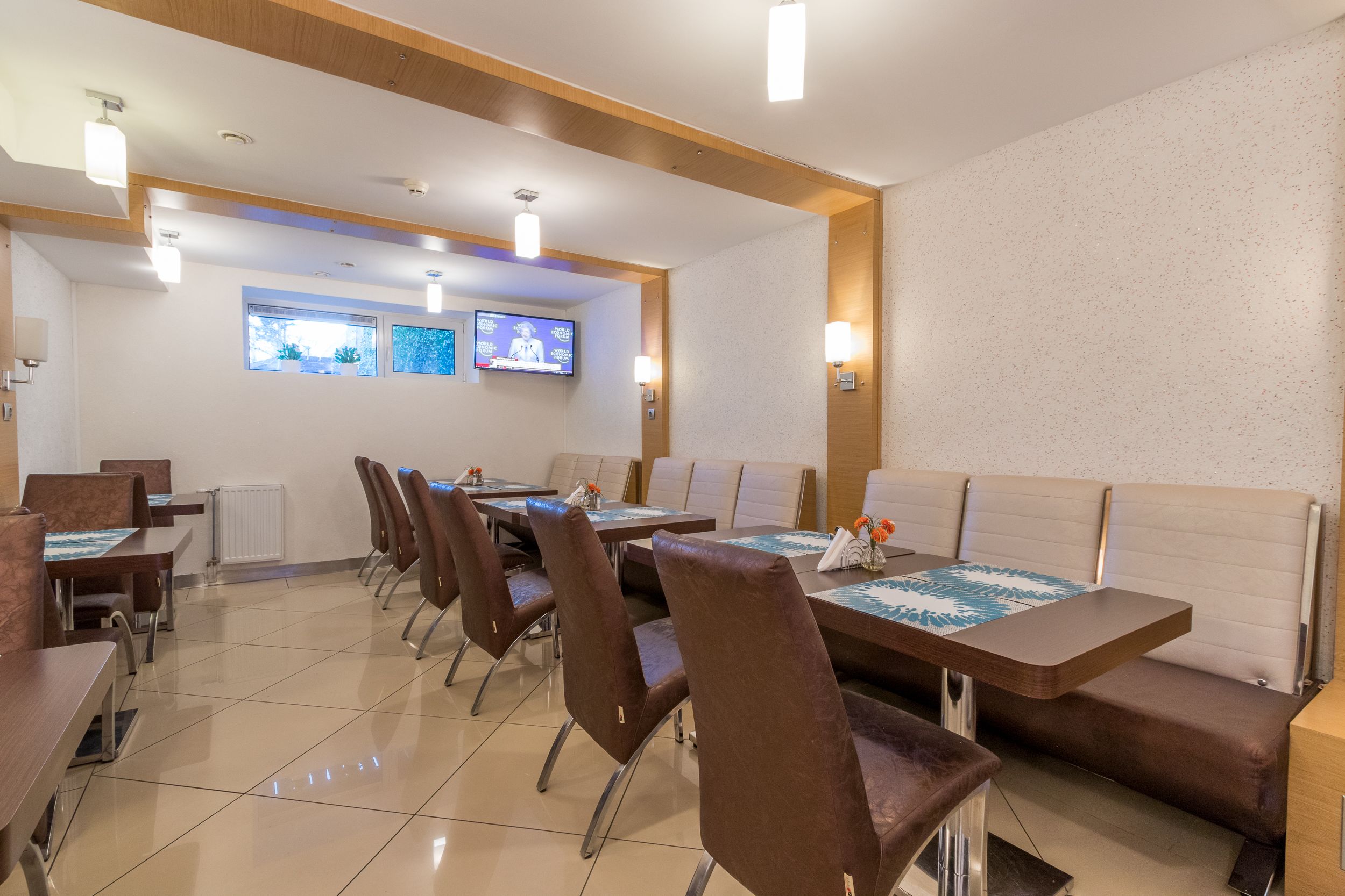 A dining area with tables and chairs, a television screen, and a window with a view.