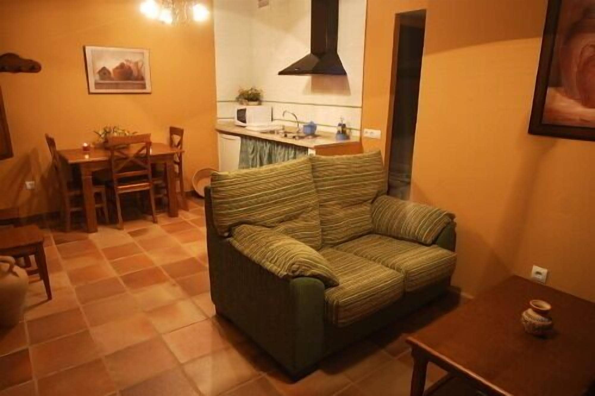 A living room with a sofa, a dining table with chairs, a kitchen area, and a painting on the wall.