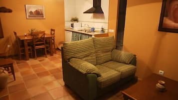 A living room with a sofa, a dining table with chairs, a kitchen area, and a painting on the wall.