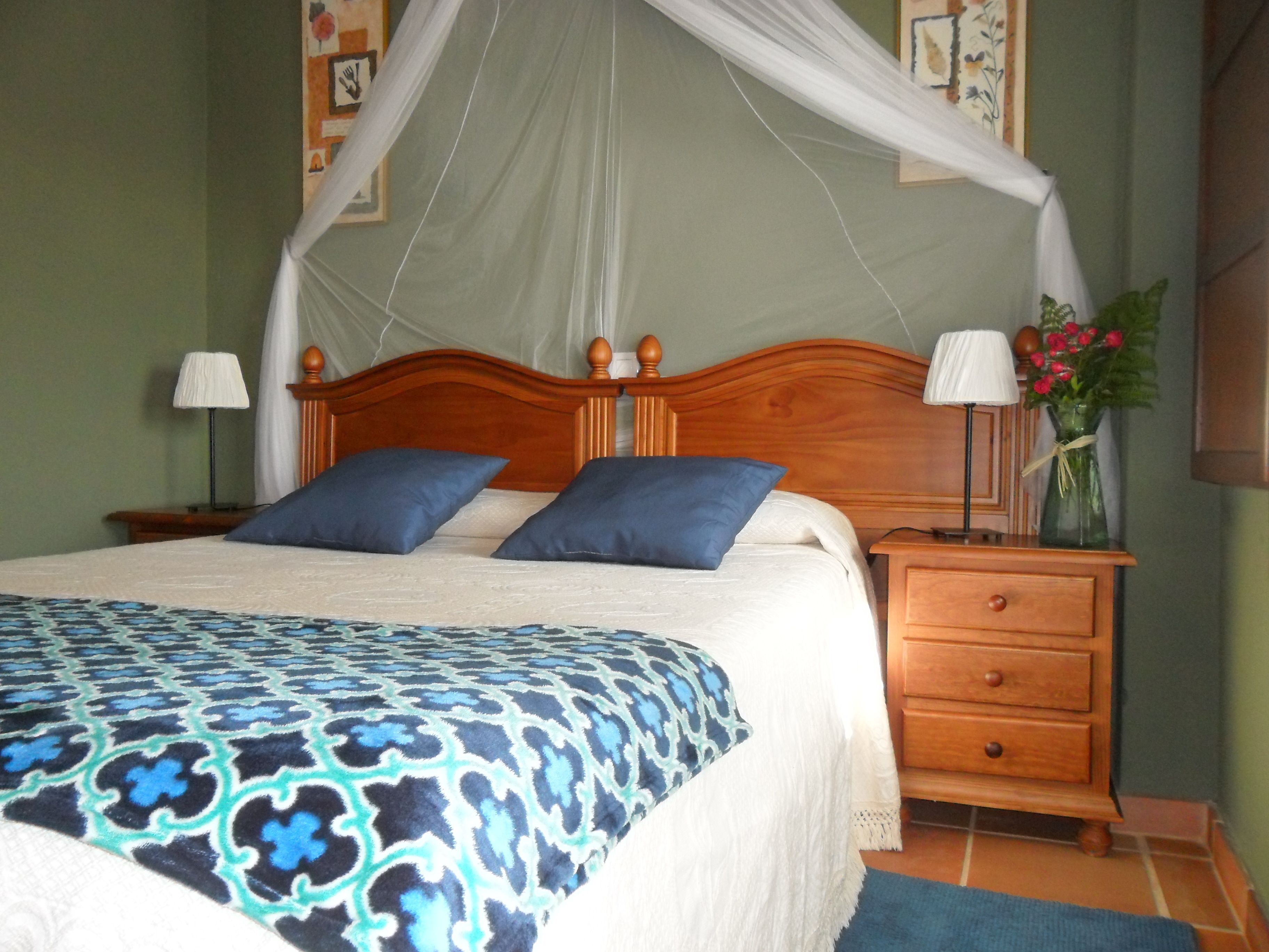 A neatly made bed with a patterned bedspread, a wooden nightstand with a lamp, and a vase with flowers.