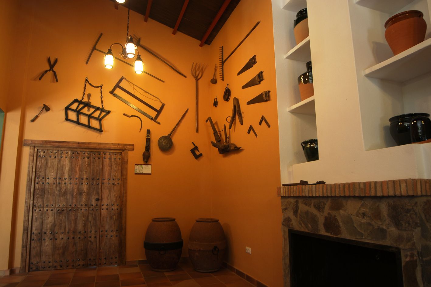 A rustic room with a wooden door, a stone fireplace, and various tools and pottery displayed on the walls.