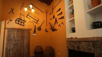 A rustic room with a wooden door, a stone fireplace, and various tools and pottery displayed on the walls.