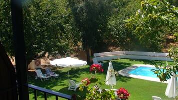 A backyard with a swimming pool, white lounge chairs, and a covered table.
