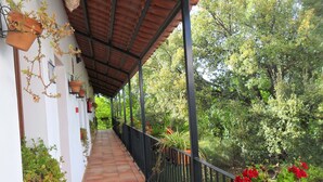 A covered balcony with terracotta tiles, potted plants, and a view of a lush garden. - Hotel Apartamento Rural Finca La Media Legua (Los Marines)