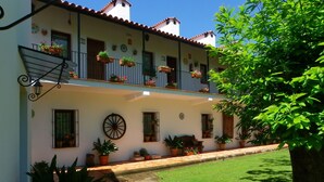 A two-story building with a tiled roof, potted plants on balconies, and a small courtyard with a lawn. - Hotel Apartamento Rural Finca La Media Legua (Los Marines)