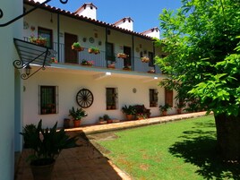 A two-story building with a tiled roof, potted plants on balconies, and a small courtyard with a lawn.