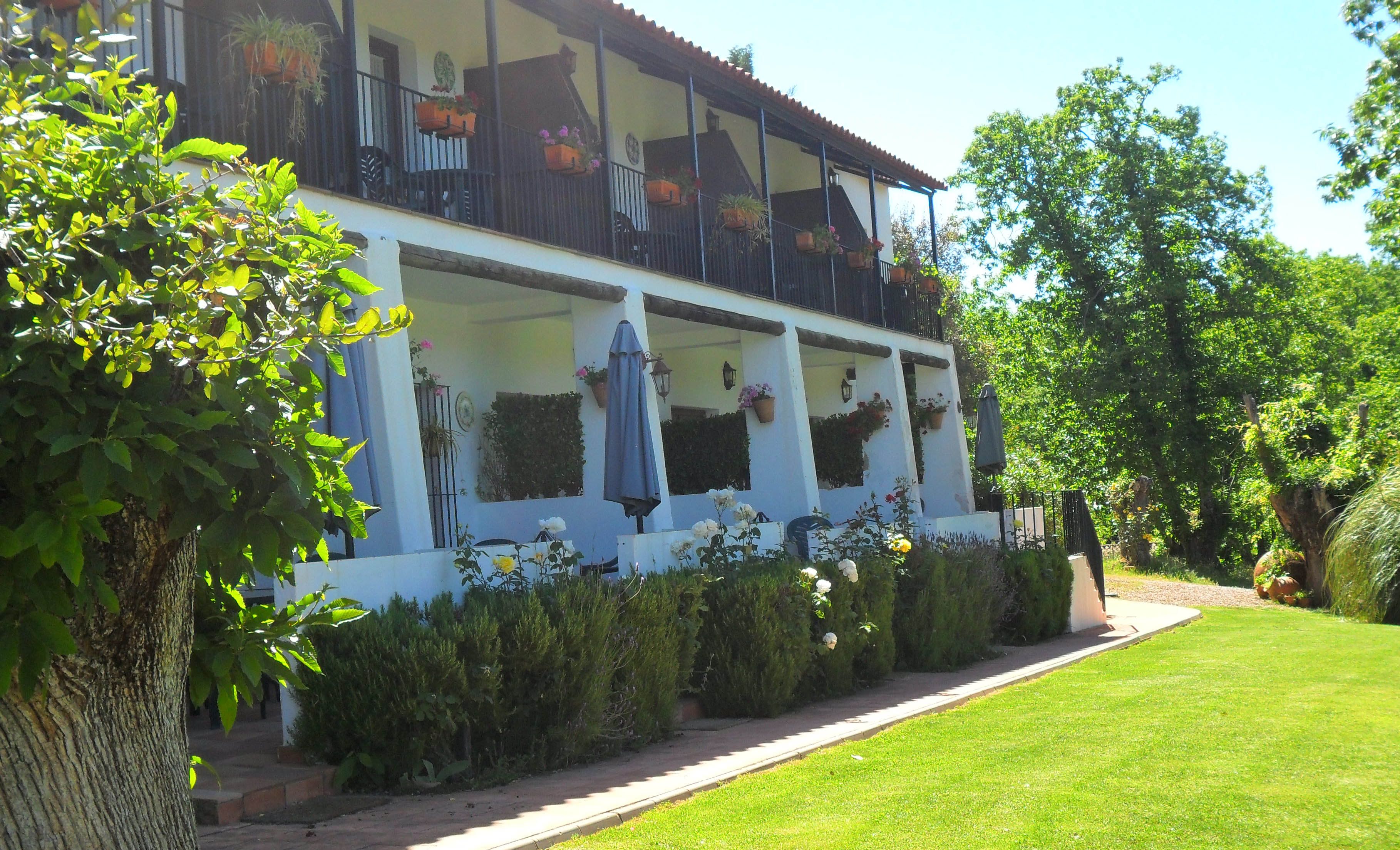 Un edificio de dos pisos con balcones, un césped cuidado y vegetación circundante.