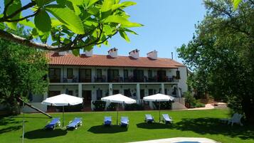 A two-story building with a red-tiled roof, a swimming pool, and lounge chairs.