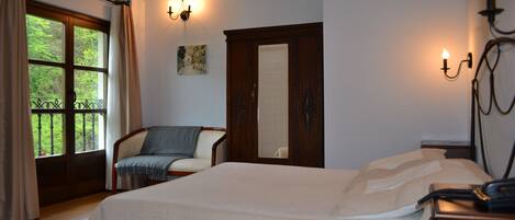 A bedroom with a bed, a chair, a nightstand with a phone, a window with curtains, and a painting on the wall.