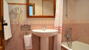A bathroom with a white sink, a mirror above it, a shower area, and a towel rack with a hairdryer.