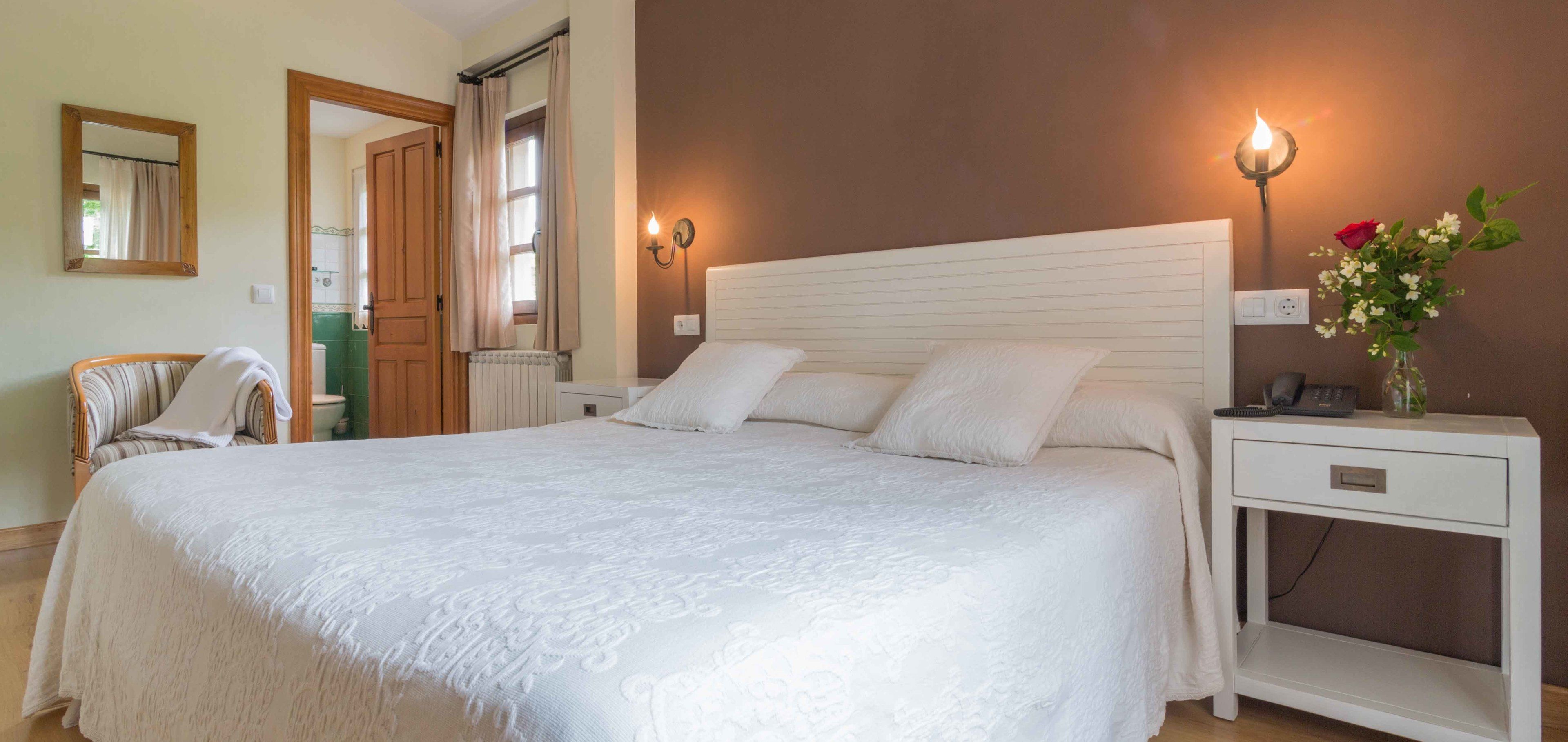 Een keurig opgemaakt slaapkamer met een groot bed, nachtkastjes, een stoel en een spiegel.