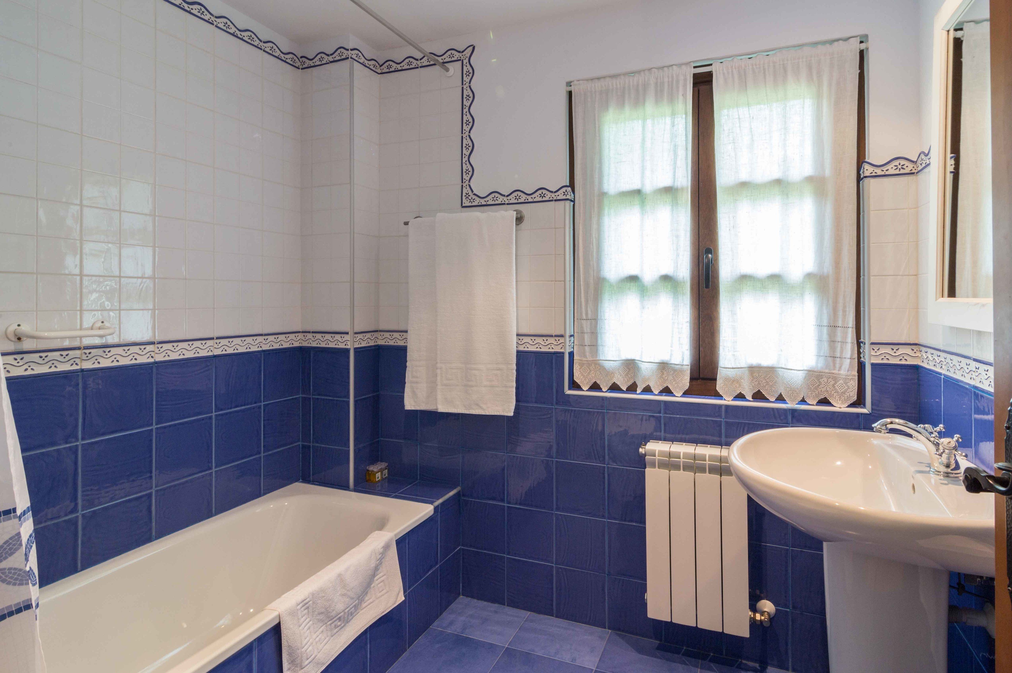 A bathroom with a bathtub, a sink, and a window with curtains.