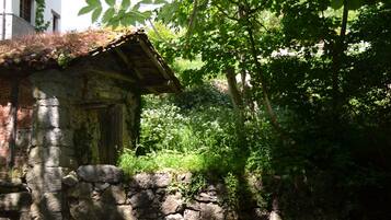 Un edificio rústico de piedra con techo de paja, rodeado de exuberante vegetación y un arroyo cristalino.