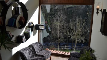Een moderne woonkamer met een grote glazen deur die uitkomt op een tuin, een boekenkast en twee gestreepten fauteuils.