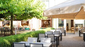 An outdoor seating area with tables and chairs, a large umbrella, and a building with glass doors in the background. - Klostergasthof Roggenburg (Roggenburg)