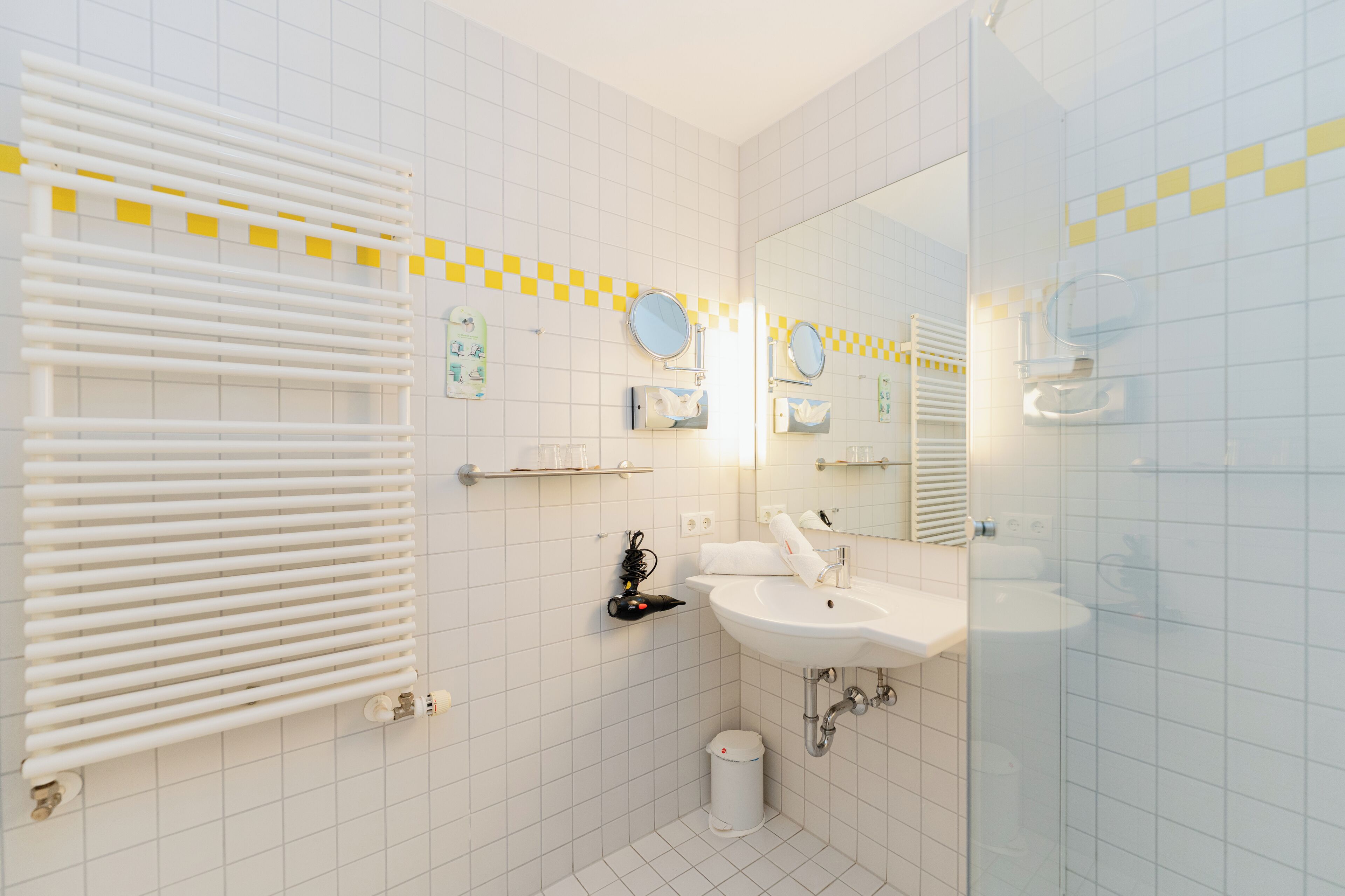 Ein Badezimmer mit weiß gefliesten Wänden, einem weißen Waschbecken, einem Spiegel und einem Handtuchhalter.