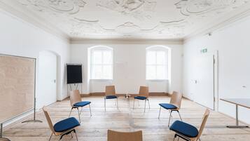Un salón de conferencias con una pizarra, un proyector y seis sillas con cojines azules.
