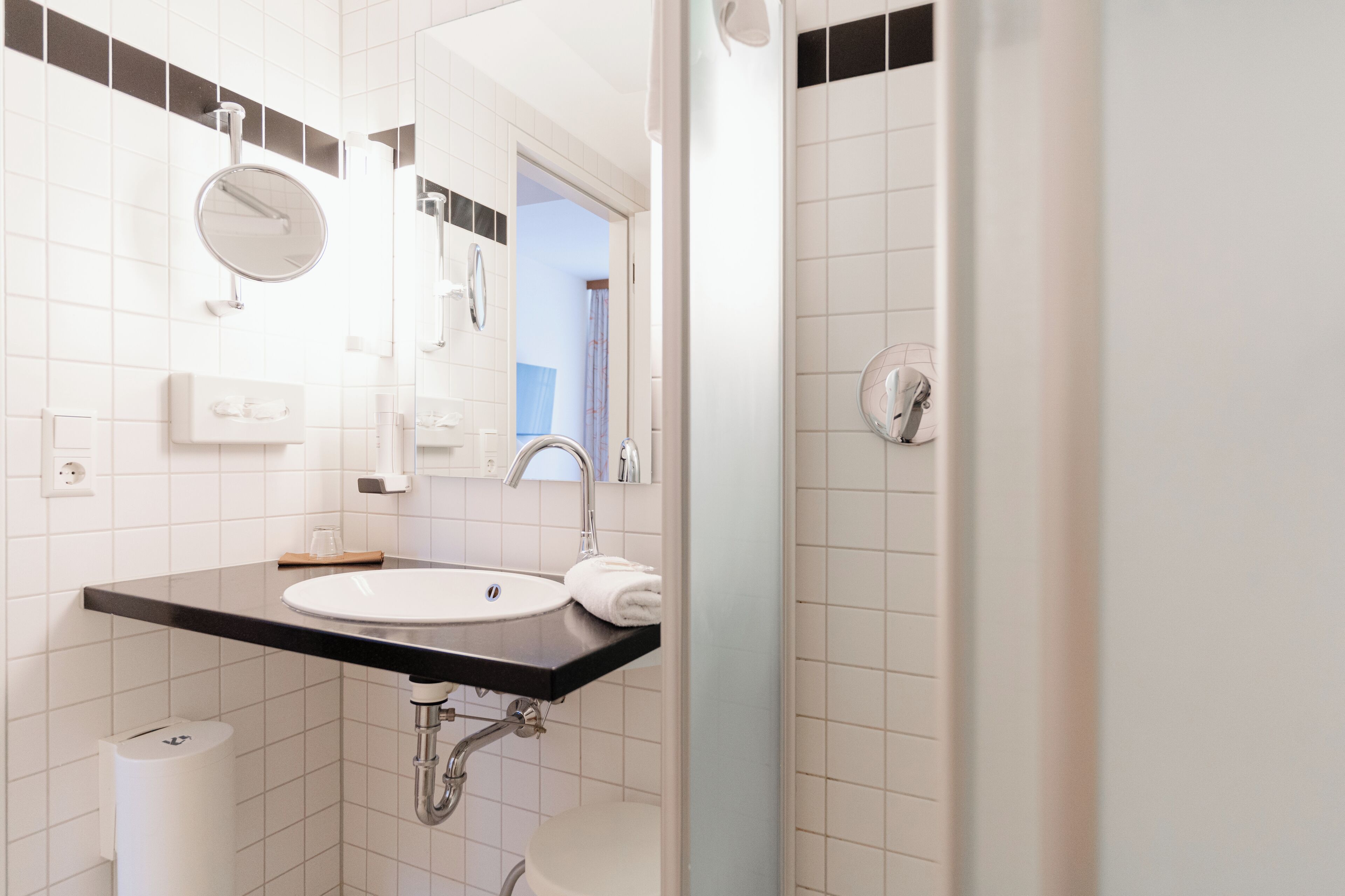 A modern bathroom with a white sink, a mirror, and a shower.