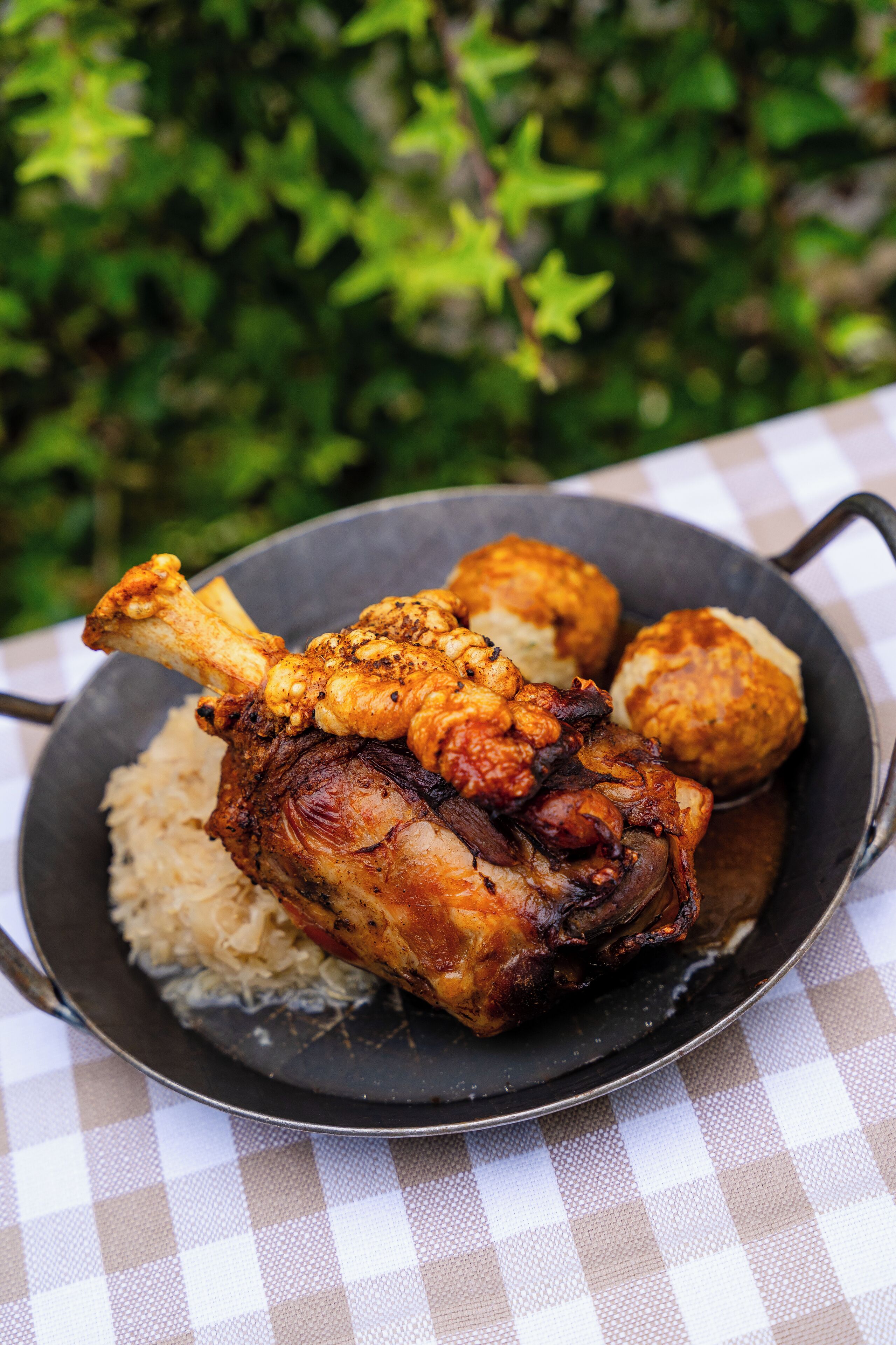 A pan with roasted meat, potatoes, and sauerkraut on a checkered tablecloth.