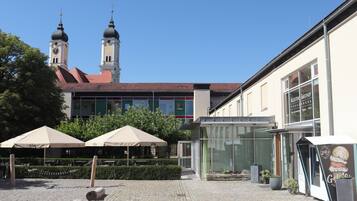 Une cour avec une église en arrière-plan, un bâtiment portant l’enseigne « Kloster Gasthof Roggenburg », et des tables à l’extérieur, protégées par des parasols.