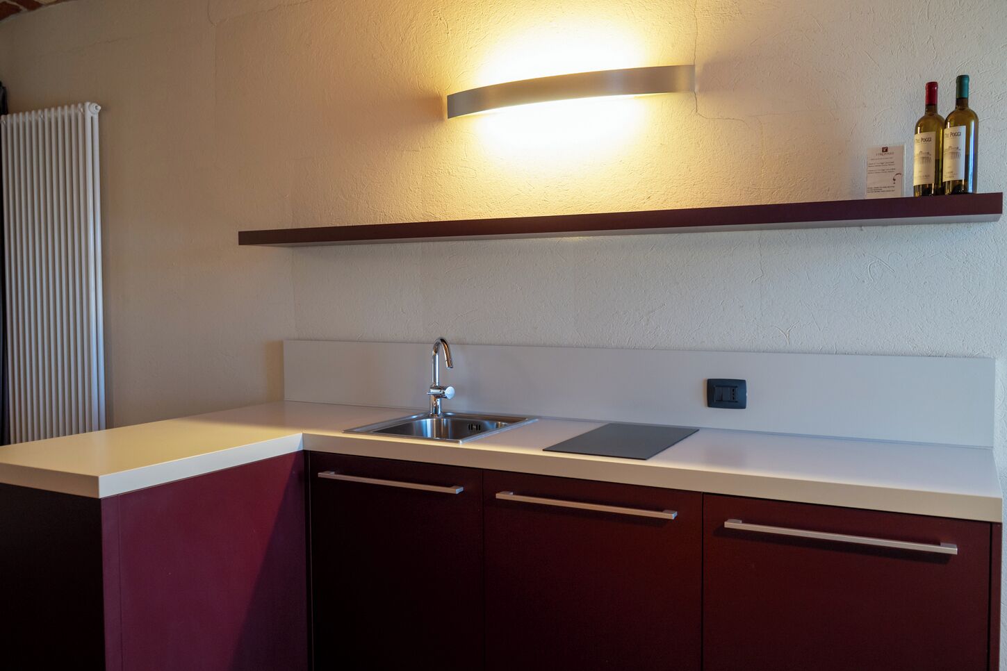 Una cocina con un lavamanos de acero inoxidable, una encimera blanca y un estante de madera encima.