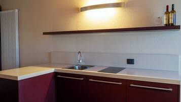 A kitchen with a stainless steel sink, a white countertop, and a wooden shelf above it.