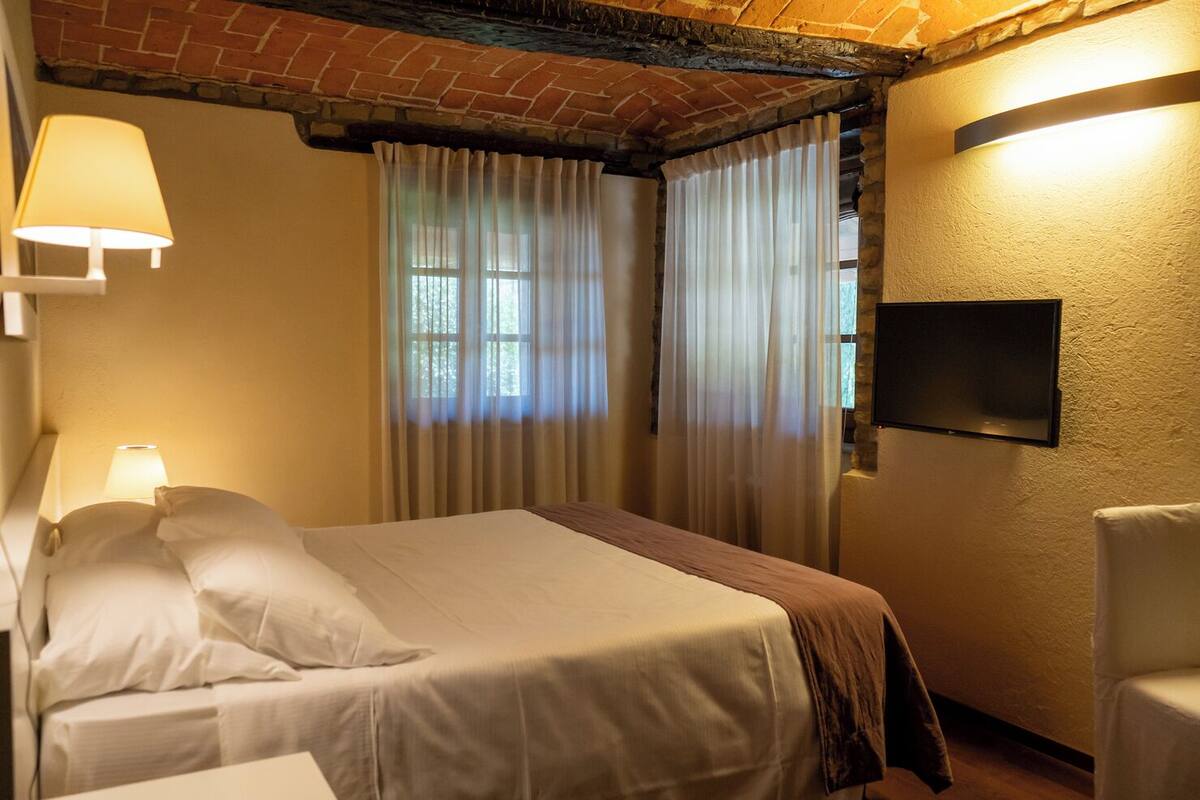 A hotel room with a bed, a chair, a TV, and curtains.