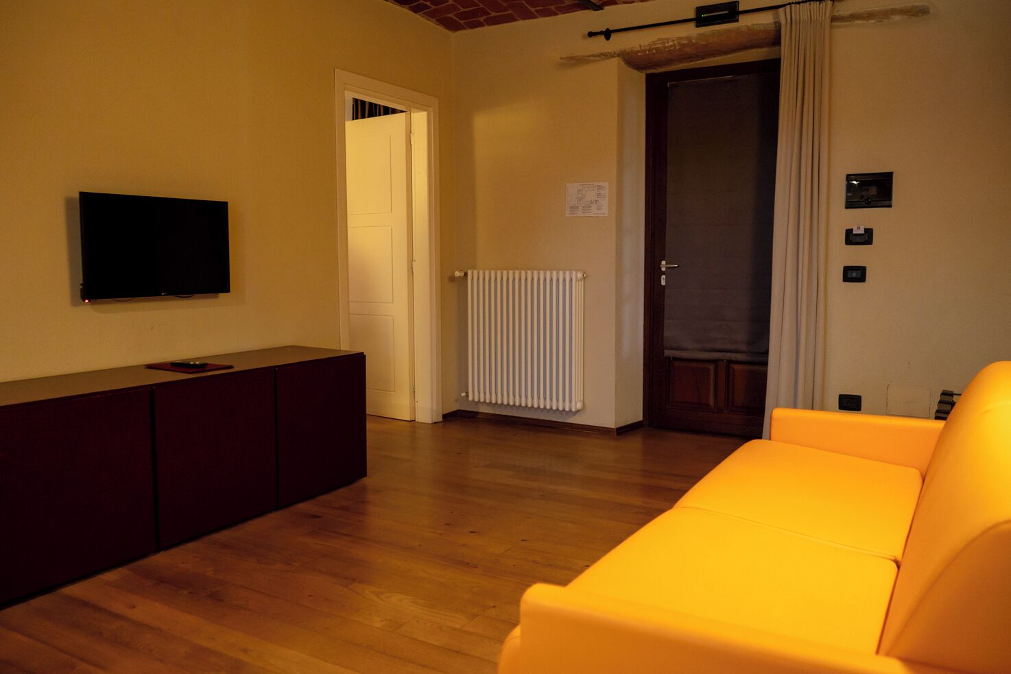 A living room with a wooden floor, a sofa, a TV, and a radiator.