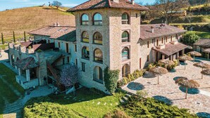 Un gran edificio de piedra con múltiples arcos y techo de tejas, rodeado de un jardín cuidado y un área de estar al aire libre.