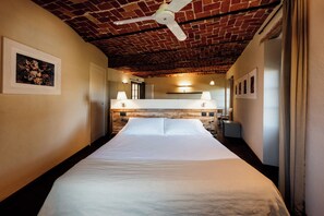 A hotel room with a large bed, a brick ceiling, and a ceiling fan. There are wall-mounted lamps and framed pictures on the walls. - I Tre Poggi Dimora di Charme (Canelli)