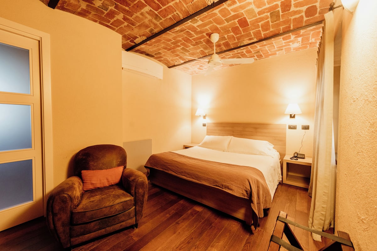 A bedroom with a brick ceiling, a wooden bed, a leather chair, and two bedside lamps.