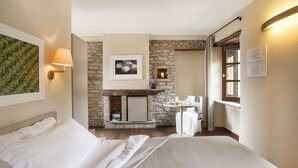 Habitación de hotel con cama, chimenea de piedra, una mesita con un florero y una ventana con cortinas.