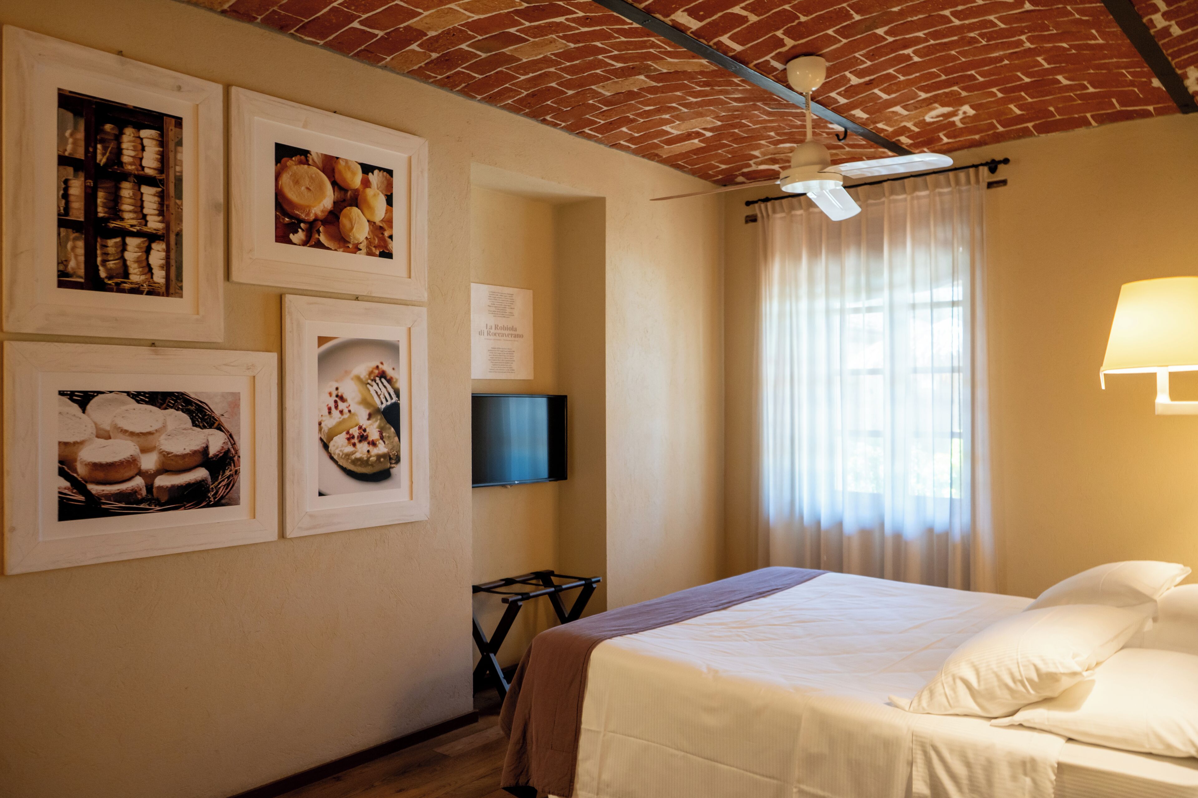A hotel room with a brick ceiling, a bed with white linens, a flat-screen TV, and framed pictures on the wall.