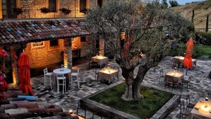 Un patio al aire libre con suelo de piedra, mesas y sillas, rodeado por un edificio de piedra con tejado de baldosas.