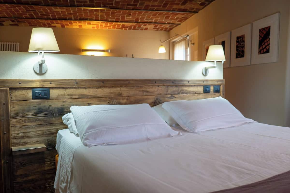 A bed with white linens, a wooden headboard, and two wall-mounted lamps.