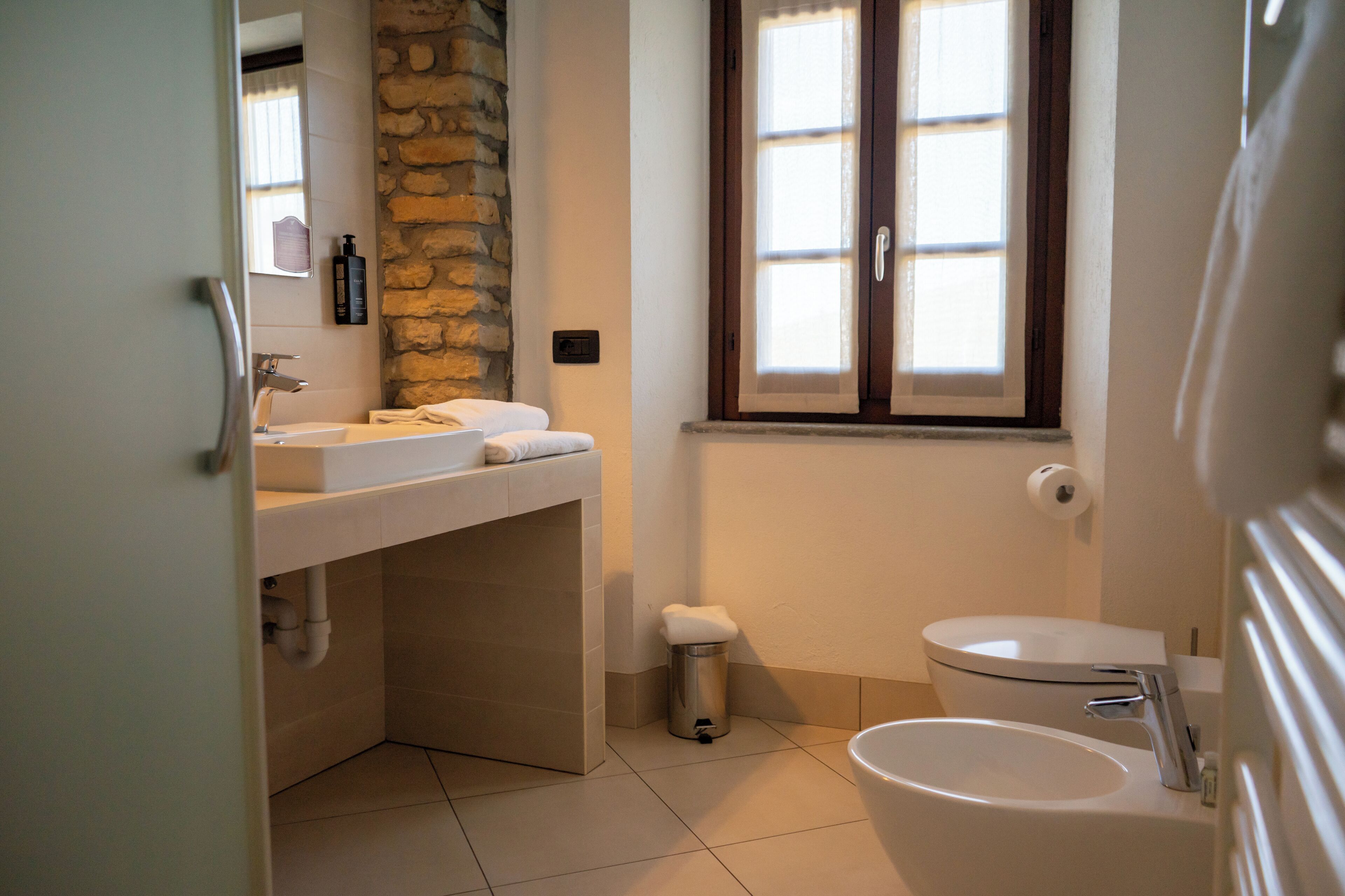 Un baño con una pared de acento de piedra, una ventana, un lavabo, un inodoro y un bidé.