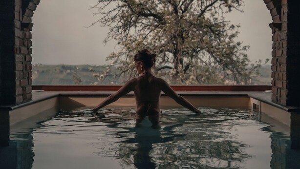 Una persona en una piscina con una estructura arqueada y un árbol al fondo.