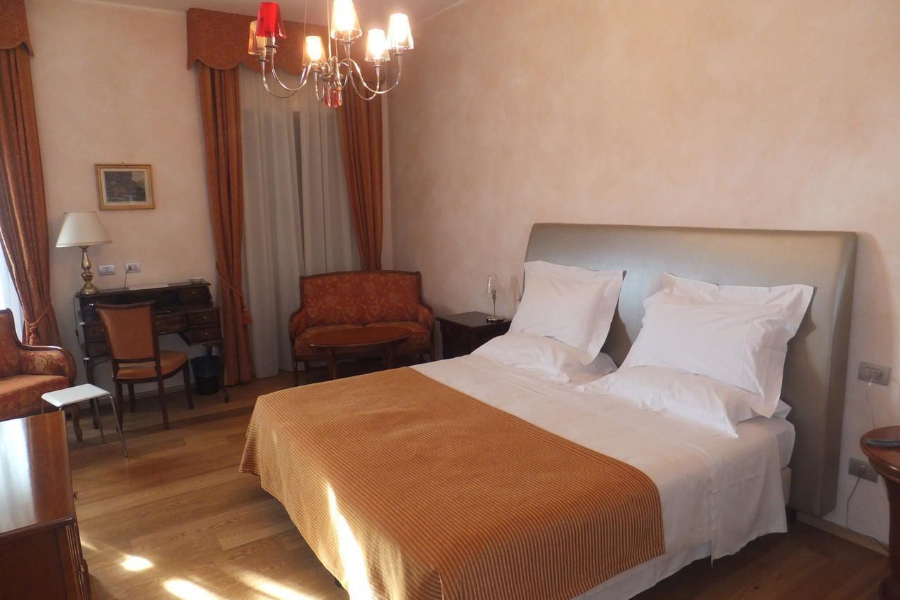 Ein Hotelzimmer mit einem großen Bett, einem Schreibtisch mit Stuhl, einem kleinen Tisch und einer roten Lampe.