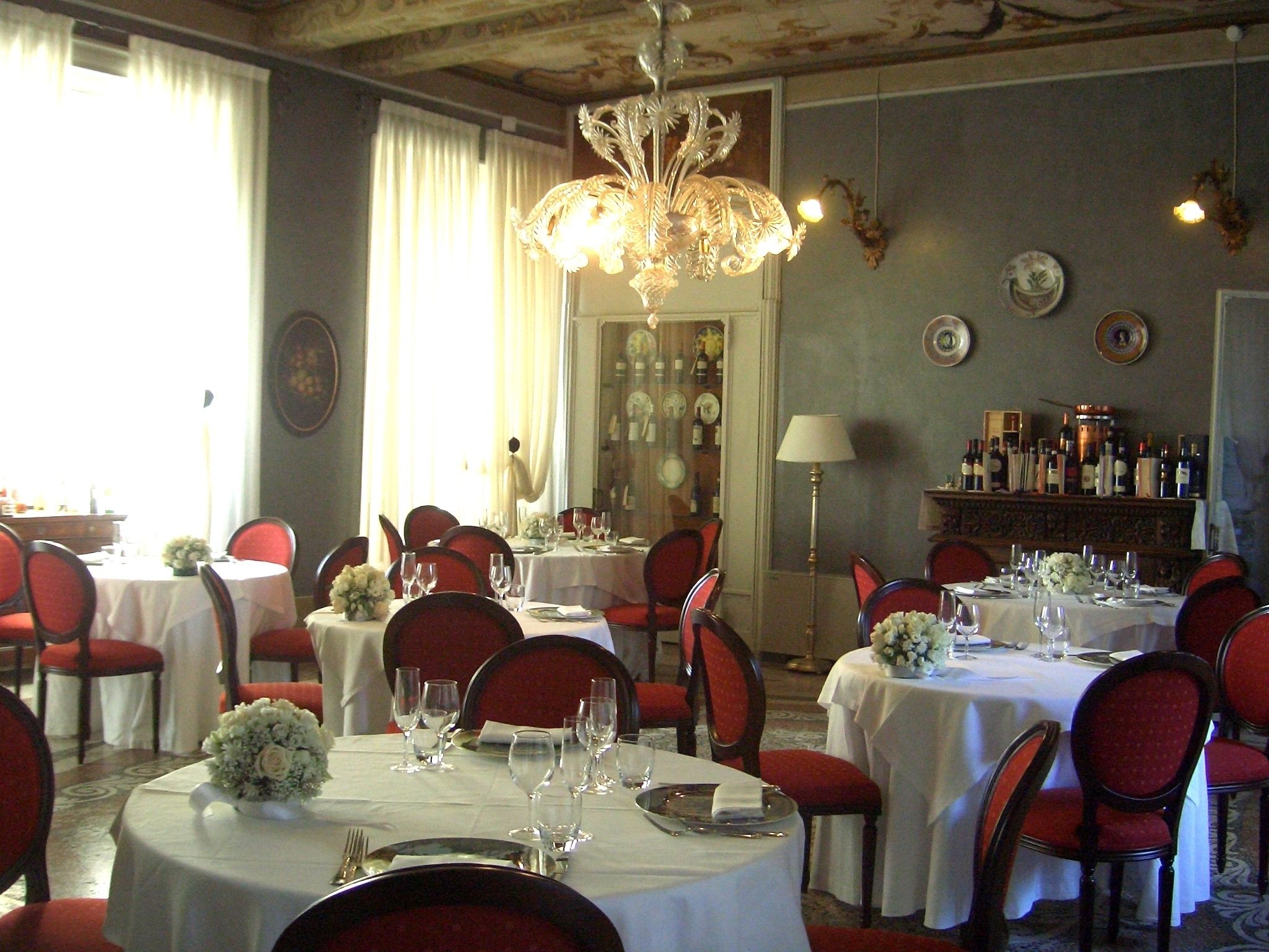Un comedor con mesas redondas, sillas rojas y manteles blancos.