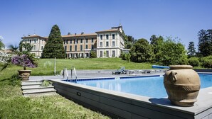 Una piscina con un jarrón grande, un césped y un edificio al fondo.
