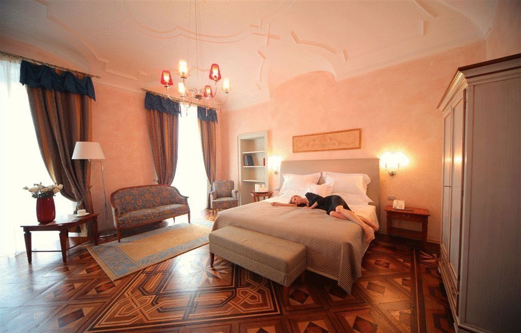 A hotel room with a bed, a sofa, a chair, a nightstand, a lamp, and a decorative rug.