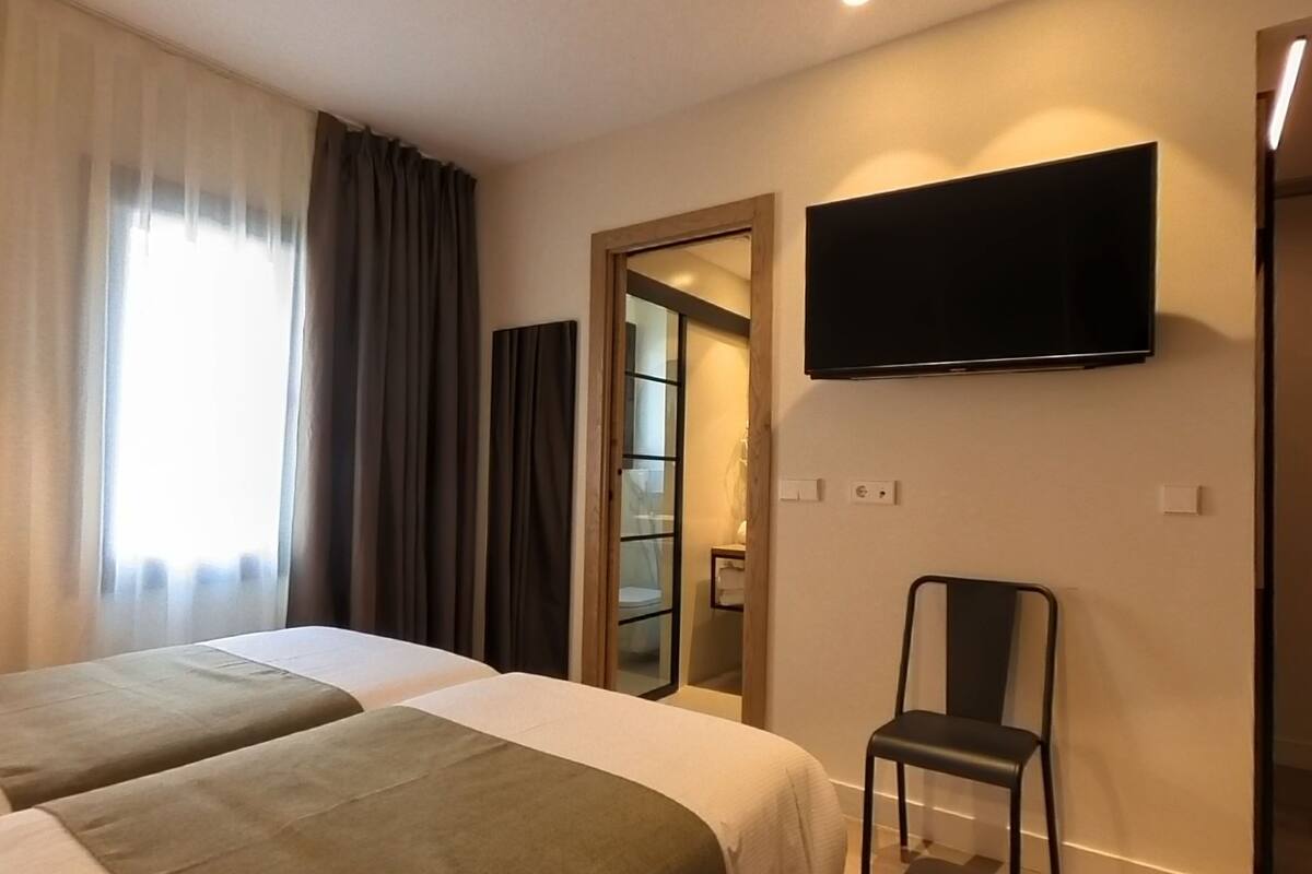 A hotel room with two beds, a TV mounted on the wall, a chair, and a door leading to a bathroom.