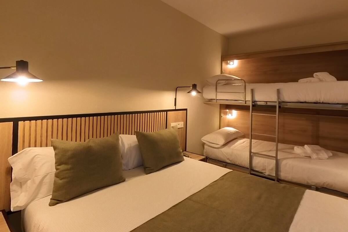 A hotel room with a bunk bed, a single bed, and a nightstand with a lamp.