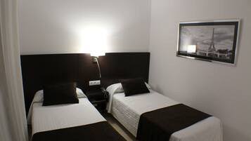 A hotel room with two single beds, a nightstand with a lamp, and a framed picture on the wall.