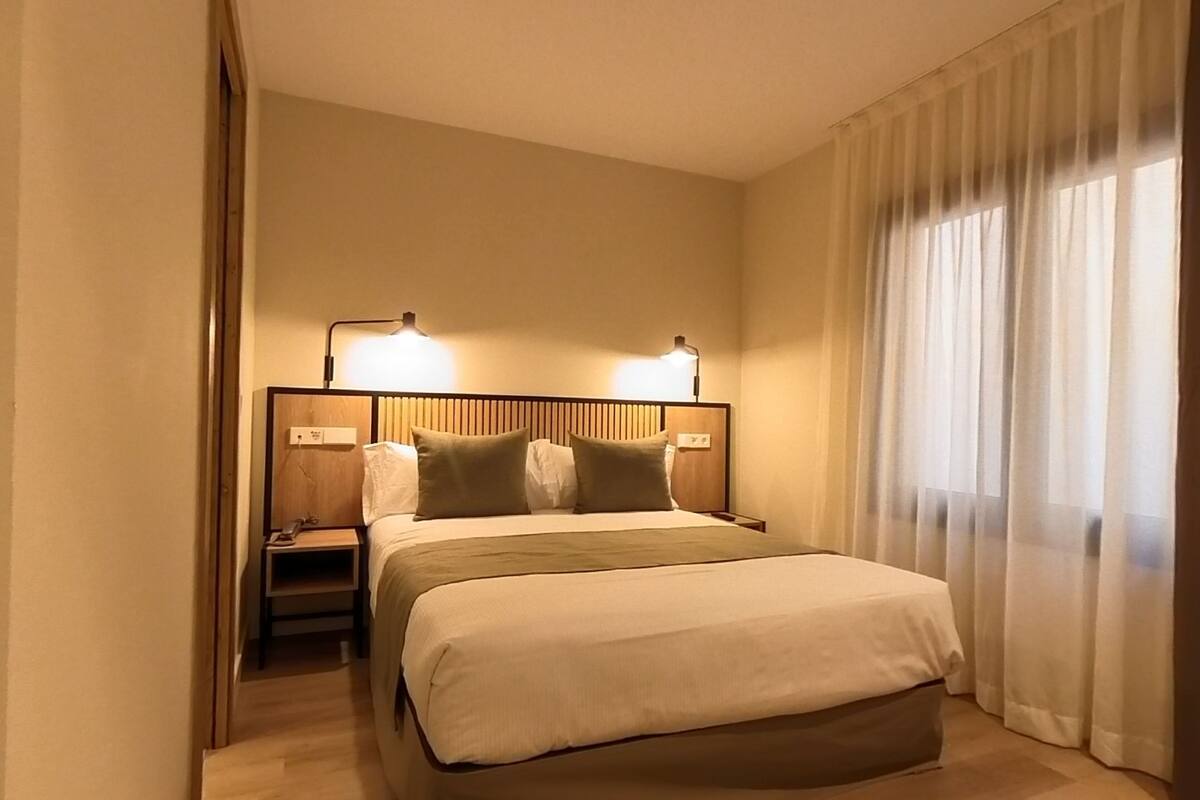 A hotel room with a large bed, bedside lamps, a nightstand, and a window with curtains.