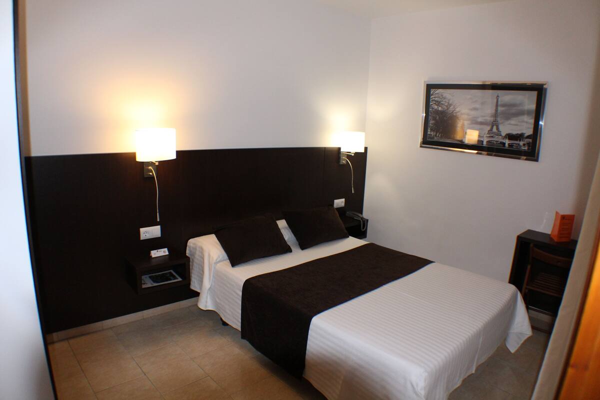 A hotel room with a large bed, two bedside tables, a nightstand, a wall-mounted TV, and a framed picture on the wall.